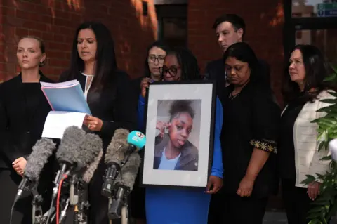 PA Media Hannah's mother, Abimbola Duyile, holds a picture of her daughter as solicitor Michelle Victor reads aloud a statement