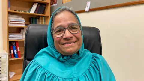A woman wearing glasses and a turquoise/green headdress called a Rida.