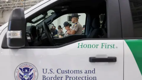 Border officers are seen through the window of a truck with a decal reading "US Customs and Border Protection" with a seal for the US Department of Homeland Security. 