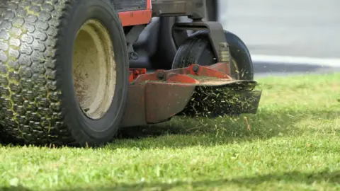 Close-up shot of a riding mower's discharge chute with focus on grass cuttings being ejected