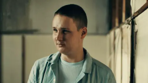 Ben Steele/BBC Denis, wearing a light blue shirt, speaks to the BBC in a warehouse