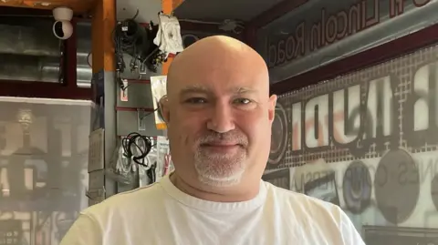 Joe Griffin/LDRS A man looking straight at the camera with a slight smile. He is standing in a shop and wearing a white T-shirt.