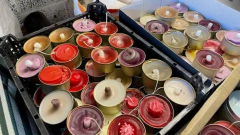 Dozens of candles in different colours fill a few boxes in a church.