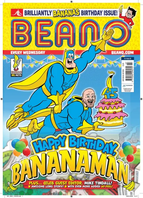 Beano/PA Wire The front cover of the Beano shows a cartoon image of Bananaman holding onto Mike Tindall as they fly through the air. They are wearing matching blue and yellow costumes. Tindall is holding a birthday cake topped with the number 45 and a banana.