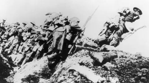 Getty Images Black and white image of British troops in full uniform, metal helmets and carrying rifles with bayonets, climbing out of a muddy trench