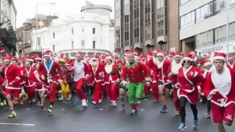 Hundreds dressed as Santas run down prospect hill, with the white Tynwald building in the background.