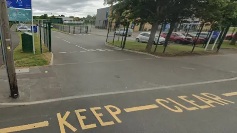 Google Part of a road with the words keep clear in yellow is at the bottom of the image. A sign that includes the words Elm Tree Primary Academy is on the left and buildings are visible in the background.