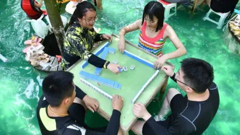 Getty Images People playing the tile-based game of mahjong in water to cool down at an attraction in Sichuan.