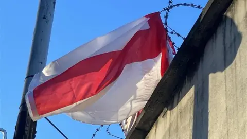 A red and white St George's flag in Lancashire, caught in barbed wire fencing and not hanging correctly.