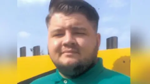 Euan Johnston, a young man with slicked back dark hair and a turquoise green polo shirt, looks into the camera. His eyes are squinting as the sun shines brightly and has a very slight smile. He is standing against a bright yellow wall.