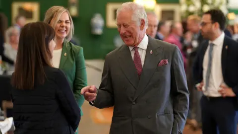 Getty Images Prince Charles speaks to guests at Dumfries House in April 2022. He is talking to two women and all three of them are laughing.