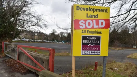 A large yellow sign above an empty, derelict car park reads 'Development land sold'