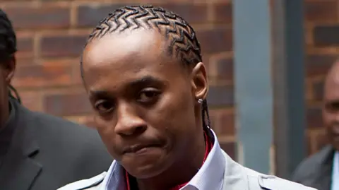 Molemo "Jub Jub" Maarohanye looks at the camera. He wears a shirt, jacket and cornrows.