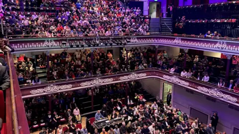 A shot of the audience sitting on various levels inside St George's Hall