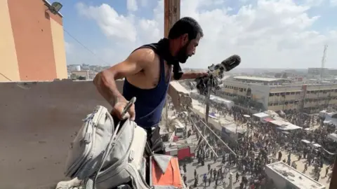 Reuters A man holds a microphone in one hand and a rucksack - both are covered in dust