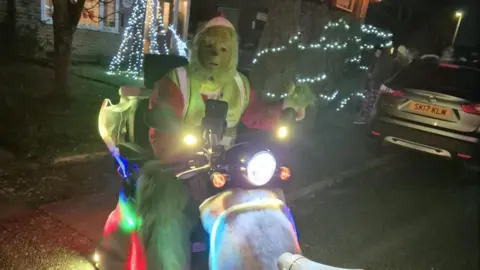Beeston Round table The Grinch on a well lit mobility scooter on a residential street