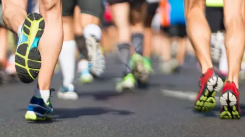 The lower legs of runners on a road surface wearing trainers