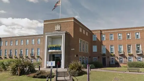 LDRS Royal Borough of Windsor and Maidenhead council building - a three-storey brick building, with a grand-looking entrance with a union flag flying over the top. There is a lawn in the foreground with some vegetation and benches in front