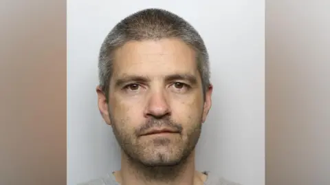 A police mugshot of Lee Boocock, who has shaved grey hair and grey stubble.