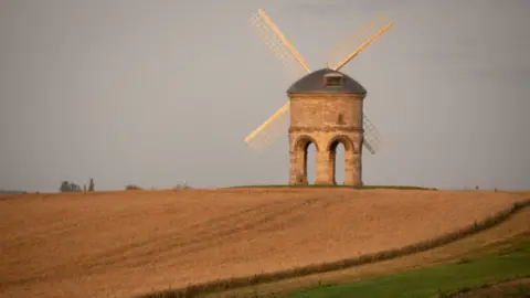 PA Media A windmill on a hilltop, with circular stone arches supporting a round tower, with metal dome roof. 