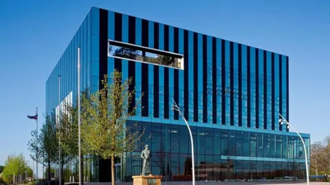 Getty Images A glass building in a cube design in the middle of a town square.