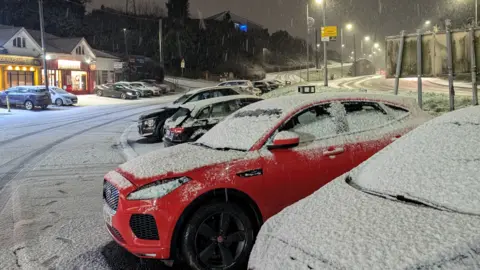 Cars covered in snow in the Four Winds area, with a dusting of snow on the ground