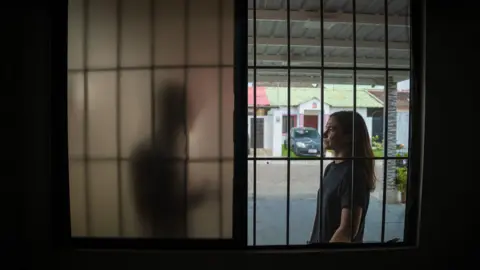 A man is demonstrated talking to a BBC journalist behind a screen, obscuring their identity