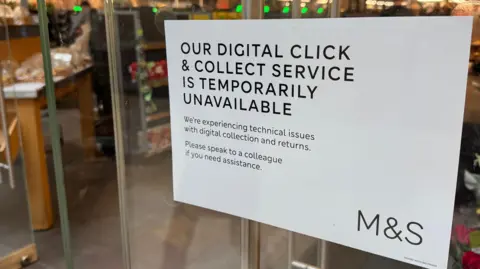 A sign on a glass door at a branch of M&S saying "the digital click and collect service is temporarily unavailable"