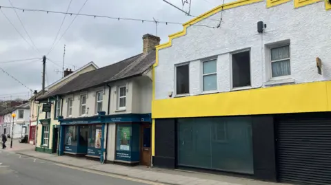 The outside of the disused building with other shops beside it