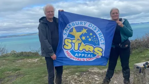 Stars Appeal Dr Helena McKeown and Peter Ewing holding a stars appeal flag on top of a cliff