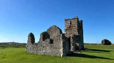 A stunning sunny day without a cloud in the blue sky. The ruins of Knowlton Church - can be seen in the centre of the image sitting on a grassy field