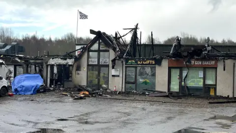 BBC The burnt-out shell of the retail unit at Inverness' Fairways. The signs of a hairdresser, travel agents and a bakers are just visible.