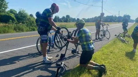 Mike Teague Two cyclists on the road bent over fixing a bike