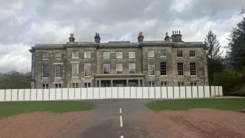 Photograph of Haigh Hall in Wigan. The image shows wooden boarding surrounding the mansion due to restoration work.
