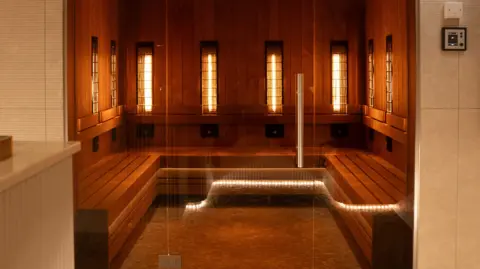 Kulture A promotional shot of the sauna at Kulture club, which is a fairly large panelled room with warm lighting, wooden benches and glass doors.