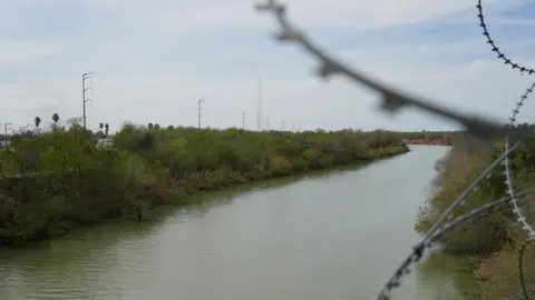 The Rio Grande river - near the Mexican city of Reynosa near the US border - is seen behind blurred spikes of barbed wire. 