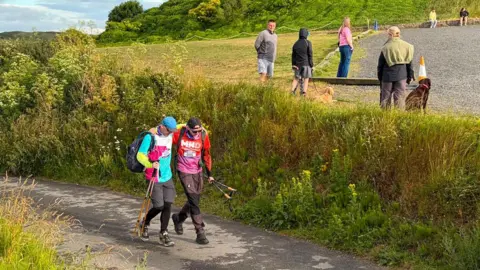 Supplied A distant shot of two men walking down a path, with a grassy bank to their left.