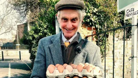 VICKI STEWARD Wilf Peddle wearing a tweed cap and blazer holding a carton of eggs and smiling