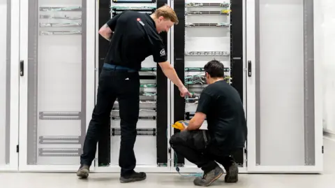 Datalec Two male engineers in black outfits work on wiring on racks in a datacentre