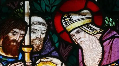 Stained glass window at St Patrick's Church in Jurby depicting St Patrick with a long grey beard and purple robes.