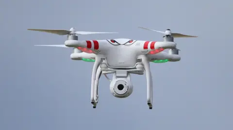 PA Media A red and white camera drone in the air.