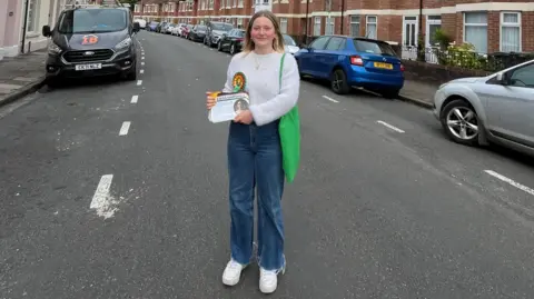 Plaid Cymru candidate Kiera Marshall, wearing a rosette on her white jumper, stands in a street