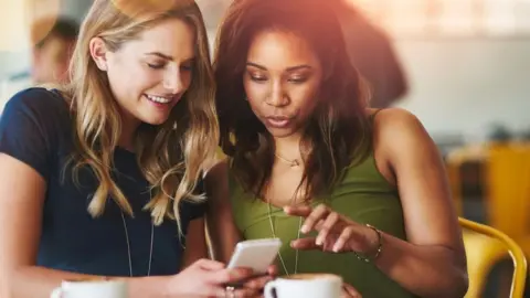 Getty Images Two women look at a mobile phone