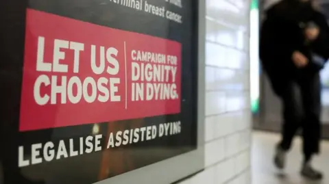 Reuters A Tube passenger walks past an assisted-dying rights billboard ahead of the parliamentary debate on Friday, in London, Britain November 26, 2024. The sign says 'Let us choose - campaign for dignity in dying' in white letter against a red background