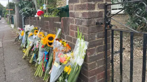 SONJA JESSUP/BBC Flowers outside the house where the bodies of a man and three children were found on Saturday