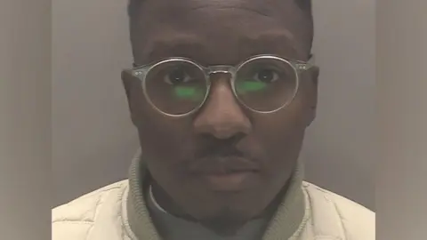 Walter Chahwanda, wearing glasses with short cropped black hair, stares straight ahead in his police custody photo
