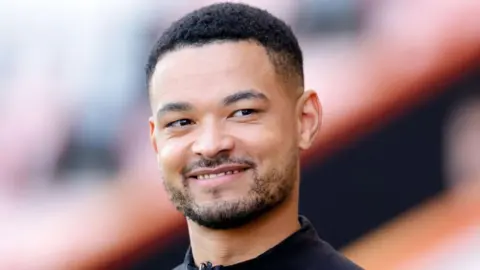 Getty Images Steven Bartlett, pictured on a visit to Bournemouth AFC in September 2023. Steven is a 31-year-old man with cropped Afro hair and a short beard. He has brown eyes and looks off camera, wearing a black shirt. 