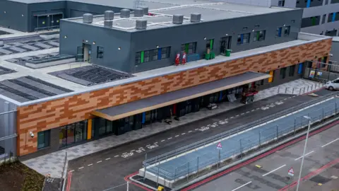 PHU Aerial shot of the outside of Queen Alexandra's emergency department. It has a brown facade with drop-off bays outside.