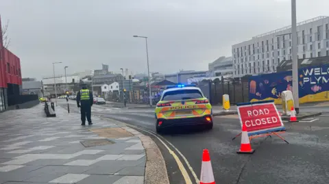 A road with a police cordon, it shows a car and an officer.