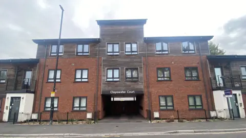 External shot of Clayewater Court, which has its name on the front of it. It is a three-storey block of flats with wooden cladding on the front.